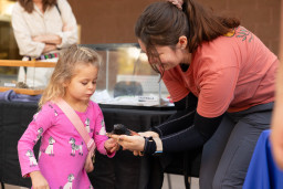 A woman holding a critter on her hand showing a little girl in a pink dress