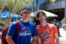 Man in blue shirt with backpack standing next to man in orange shirt at the Red Mountain Campus.