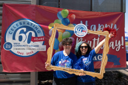 Two students holding up photo frame in front of happy birthday sign.