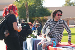 Student wearing black shirt and pants talking to a student with a guitar.