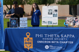 Man holding a laptop standing next to a girl with long brown hair at the PTK information table