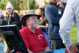 MCC employee wearing a red polo shirt sitting at a table talking to people