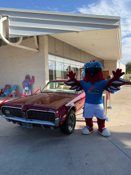 Thor is costume standing next to a vintage red sports car.