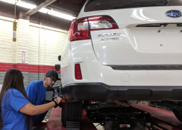 White Subaru on car lift with 2 students looking at car