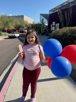 Child holding popsicle and balloons at the 60th finale event at the Red Mountain Campus