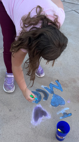 Child painting "I love MCC" on the sidewalk