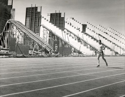 A runner strides by the Football Stadium under construction at Southern & Dobson, 1967-68