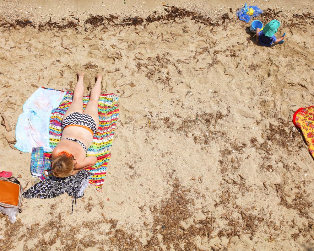 Photograph of a woman sunbathing on a beach in Italy, with a child playing nearby.