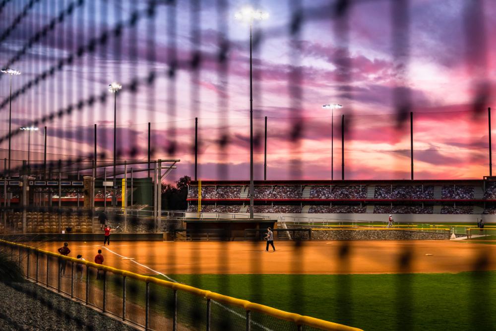 Photograph of baseball field at sunset behind a fence.