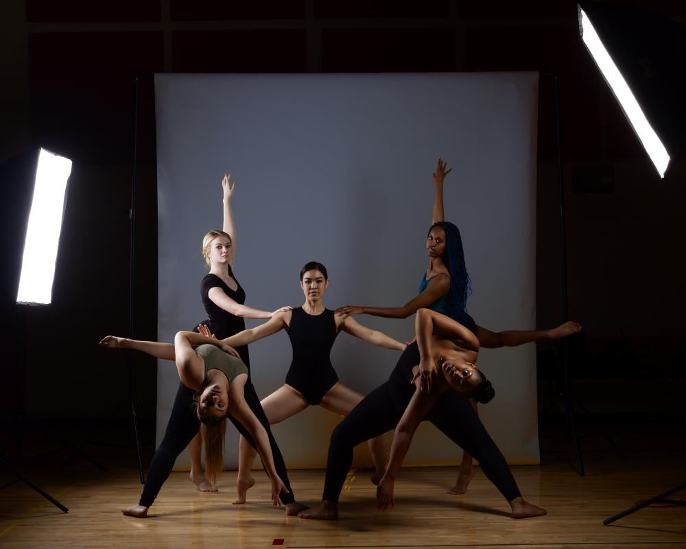 Photograph of 5 dancers in a studio with lights, in front of a backdrop.