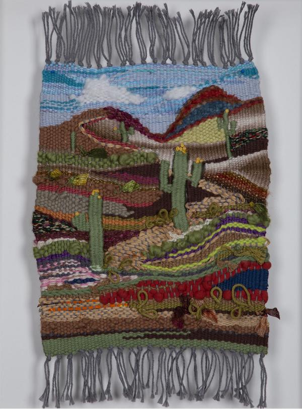 Weaving of a desert landscape with cacti and mountains in the background.