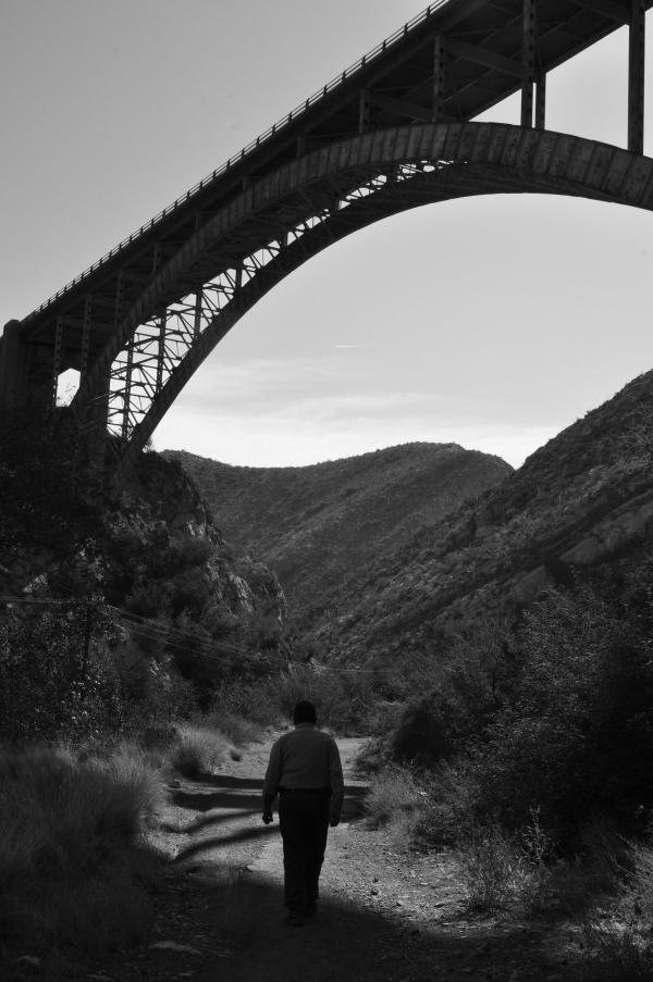 Photograph of a figure walking under a bridge.