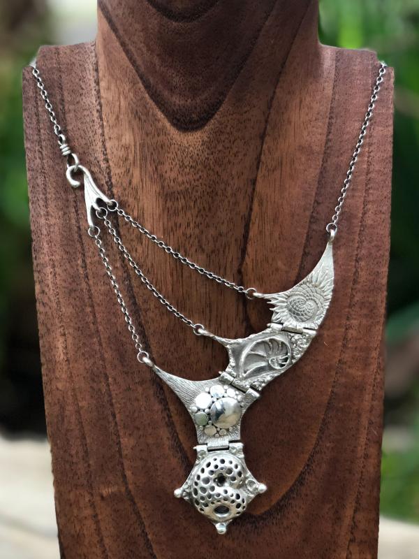 Silver necklace on a wood stand.