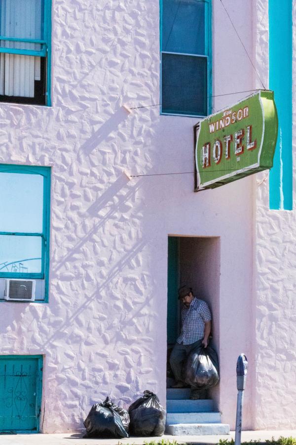 Photograph of a pink motel with turquoise windows. A man is taking out the garbage.