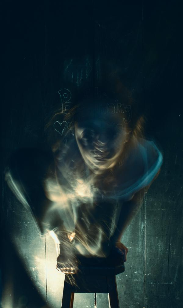 Digital photograph of a blurry figure in a dark room ascending the stairs.