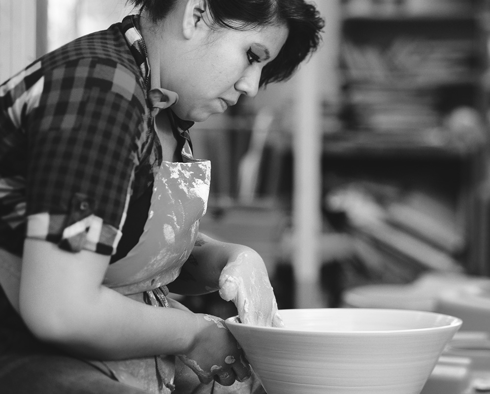 A student forming a pot from wet clay.