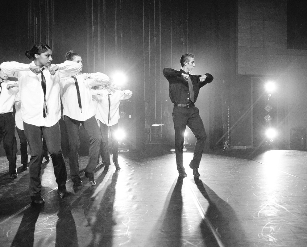 A group of dancers with elbows up on stage.