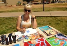 A painter displays several canvases on a table outside.