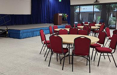 A grouping of tables and chairs in a large room with flags in the background.