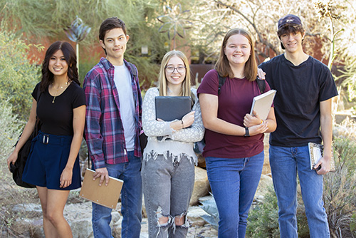 Five young students outside holding notebooks.
