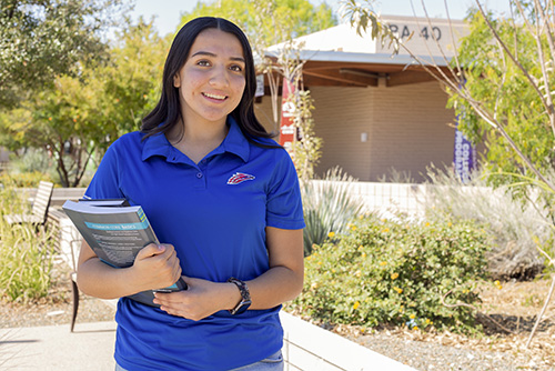 A student holding textbooks outside on campus.
