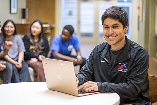 A student smiles while working on a laptop.