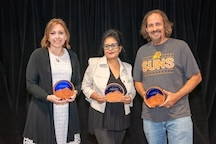 Maralena Cicchetti, Rupanjana Sengupta and Czar Getz in front of a black curtain; each is holding a round plaque of wood and glass with a desert landscape and a Saguaro cactus. The plaques have the words 2026 Outstanding Adjunct Faculty, their name and Mesa Community College. 