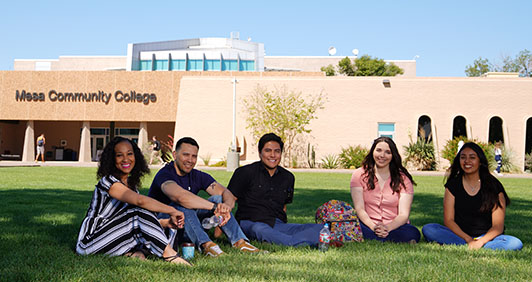 A group of five students sitting on a campus lawn