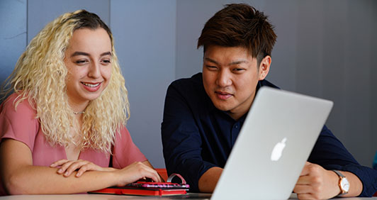 Two students looking at a laptop while seated