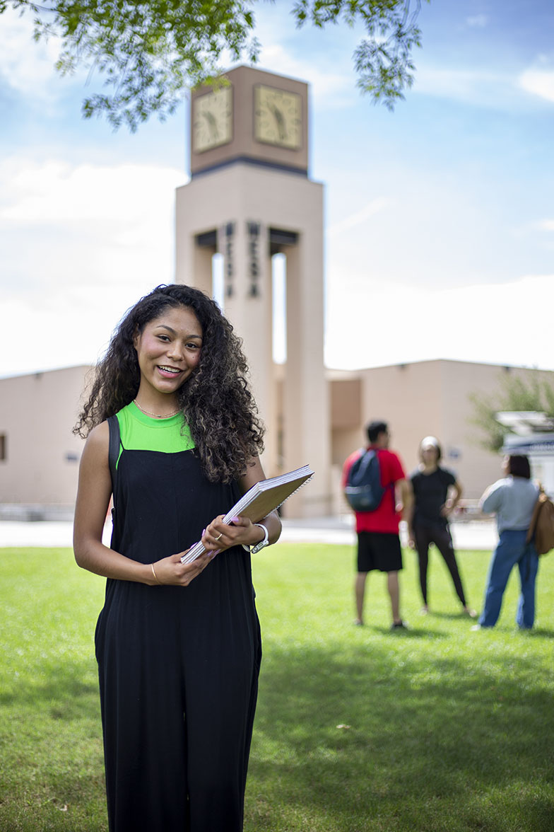 A female student holding a notebook in front of the MCC clock tower