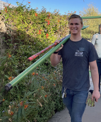 A volunteer carries two shovels outside.
