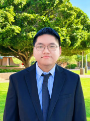 Albert Lin in a suit posing in front of mature trees.