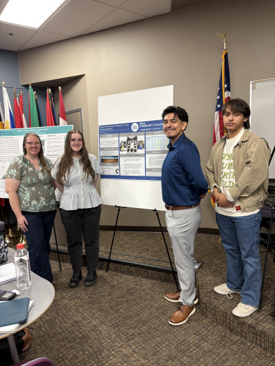 Four students standing next to research poster boards.