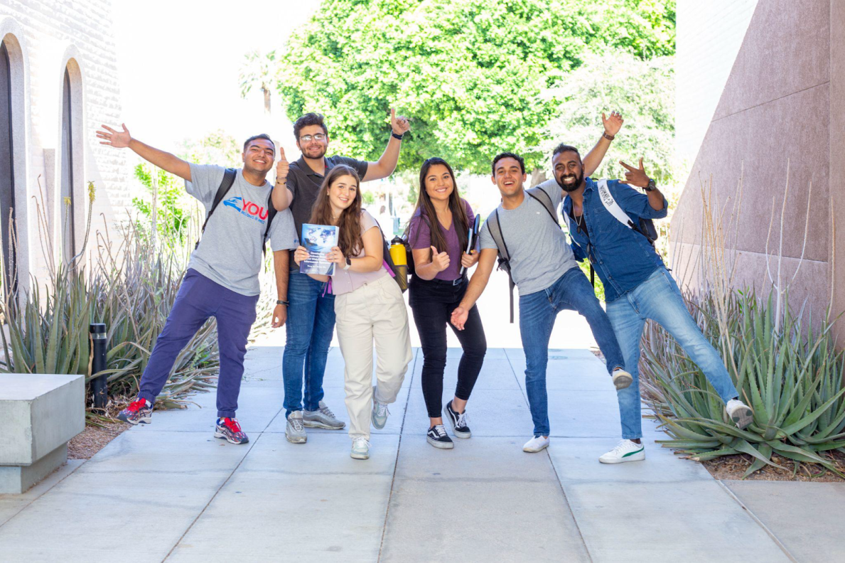 Six international students smiling, making hand gestures, and holding books.