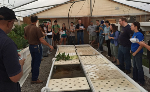 A group listening to a man in a greenhouse.