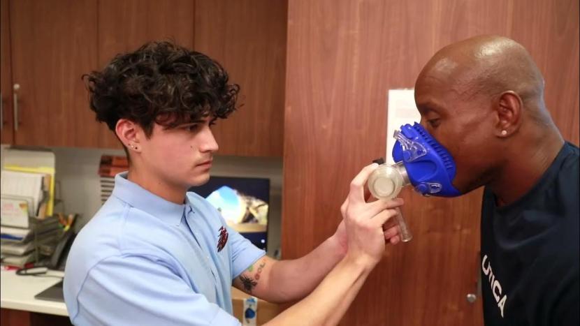A male student holding a breathing mask on the face of another man