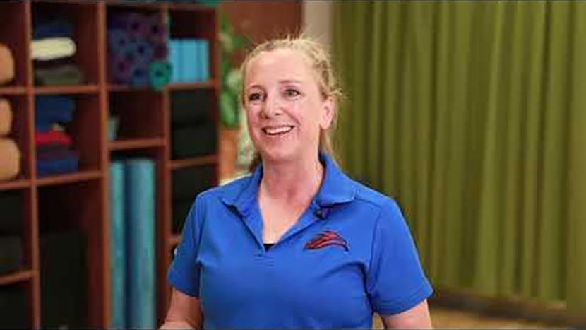 A female student facing the camera with yoga mats in the background