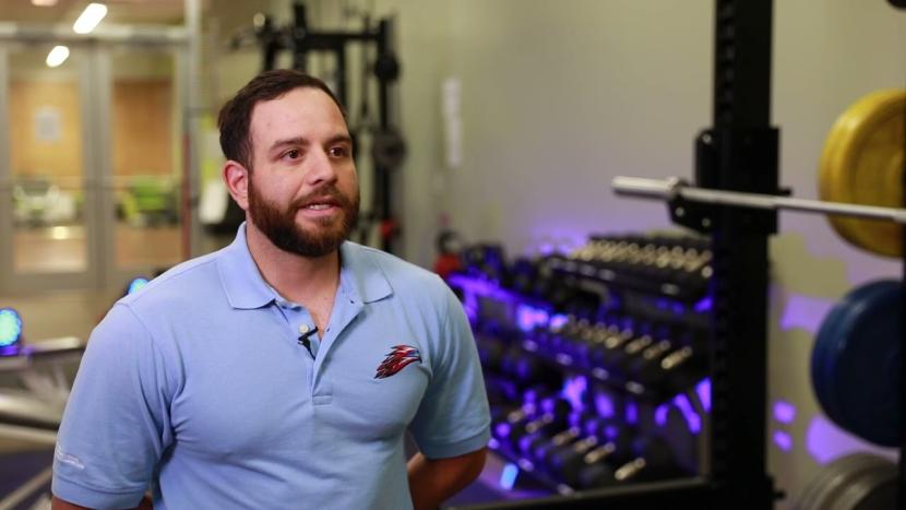 A male student facing the camera with exercise weights in the background