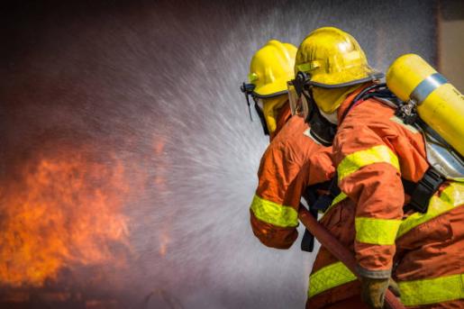 Closeup of two firefighters spraying water on a fire.