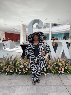 Sheena Adams wearing a black and white outfit standing in front of fashion week sign.