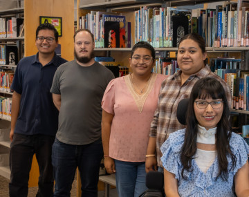Five students in front of library book shelves. 
