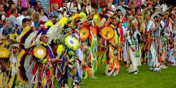 Group of American Indian performers in colorful traditional clothing.