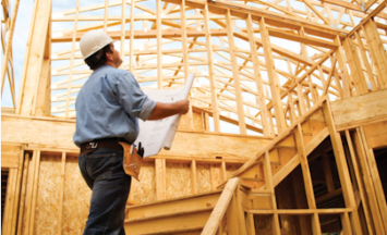 person at construction site with blueprint looking at building frame