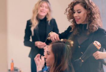A stylist blowdrying a client's hair while a third person observes