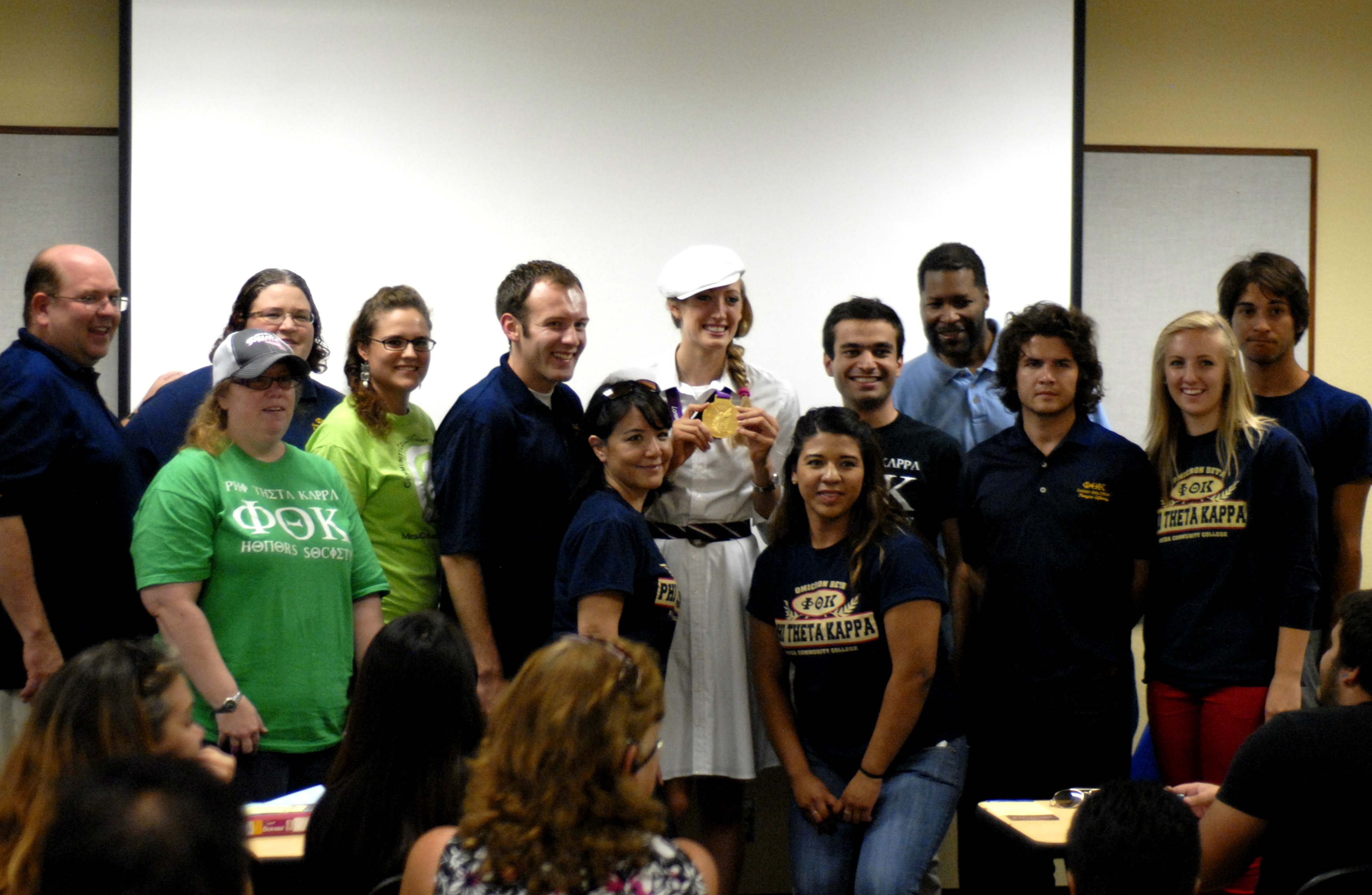 Breeja Larson holding a gold medal surrounded by PTK members in a classroom.