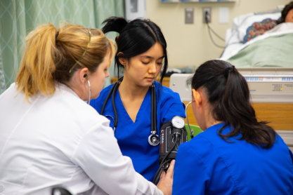 A nurse instructing two students on use of a blood pressure cuff