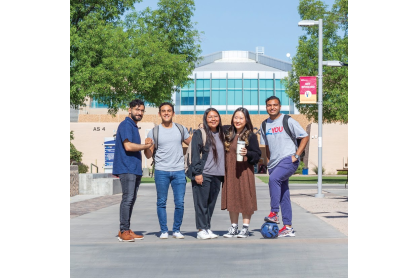 group of five college students standing in front of buildings and trees