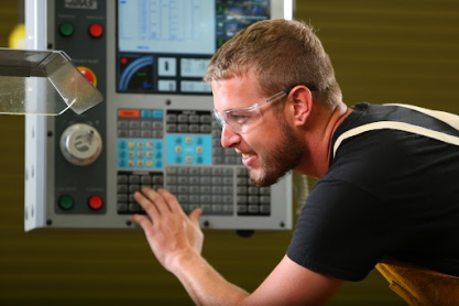 Smiling Mesa Community College student hunched over looking in a machine while keying codes on a control panel. 