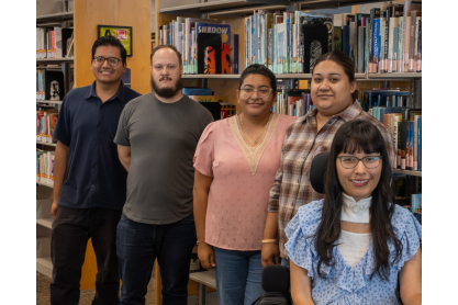 Five students in front of library book shelves. 