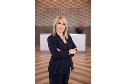 Francis Tesmer in a black suit posing in her salon with ROLFS logo behind her.